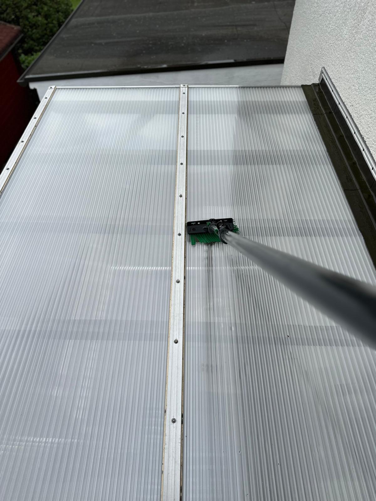 Reinigung eines transparenten Daches mit einem langen Besen.