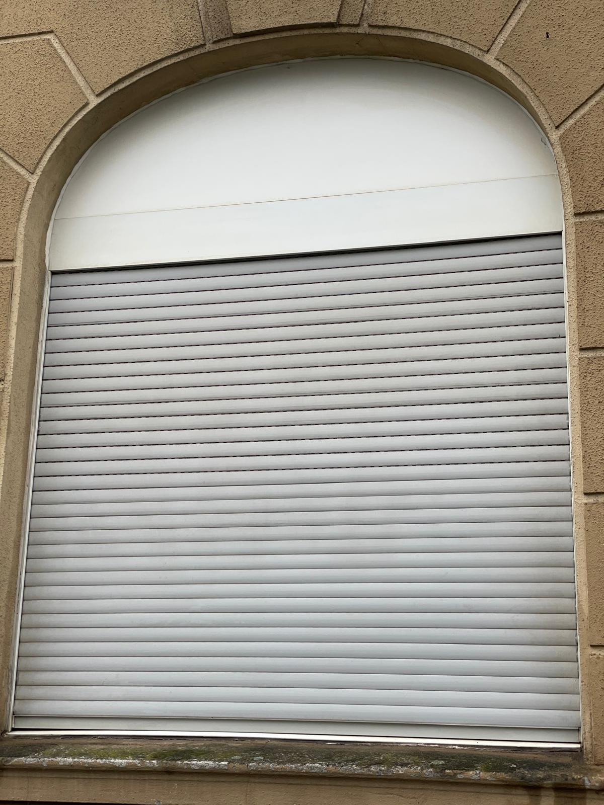 Graue Rollladen in einem Bogenfenster mit hellem Rahmen.