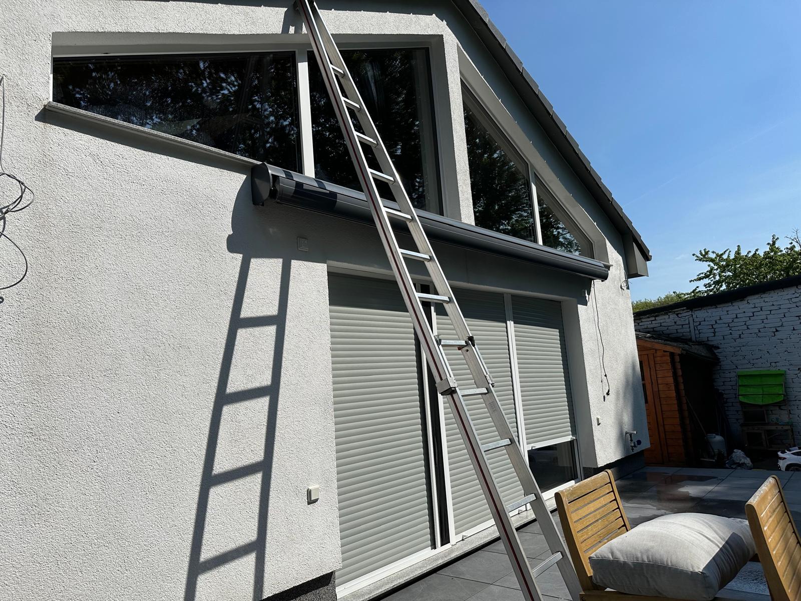 Eine Leiter steht an der Wand eines modernen Hauses mit großen Fenstern.