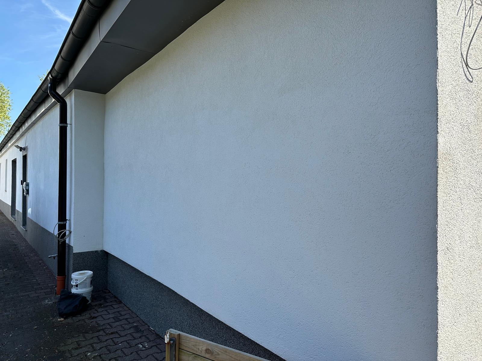 Seitenansicht eines Gebäudes mit frischer Fassade und grauem Sockel.