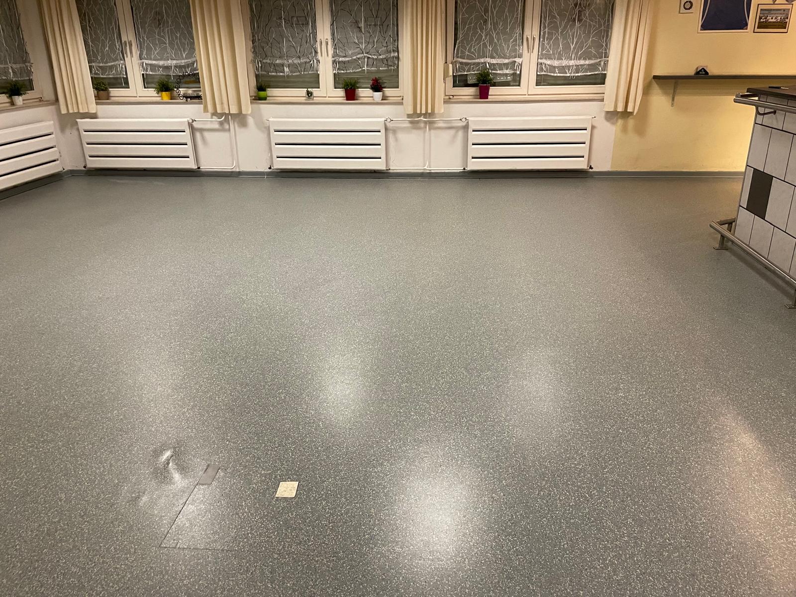 Ein Raum mit grauem Boden und Fenstern mit Vorhängen.