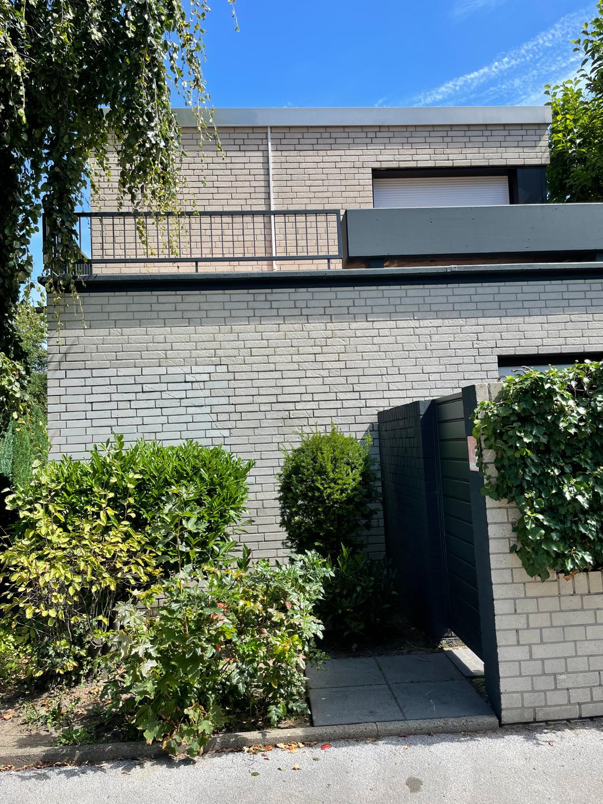 Modernes Haus mit Garten und Zaun, blauer Himmel im Hintergrund.