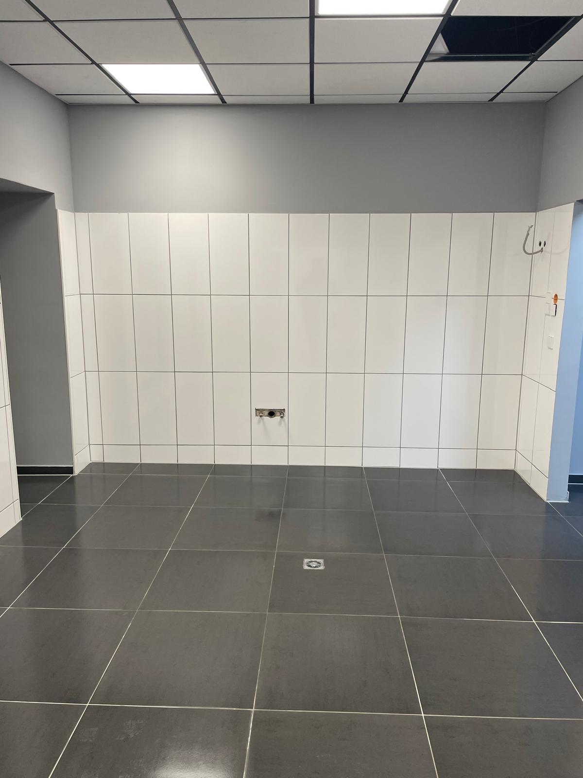 Leerer Raum mit grauen Wänden und schwarzen Fliesenboden.