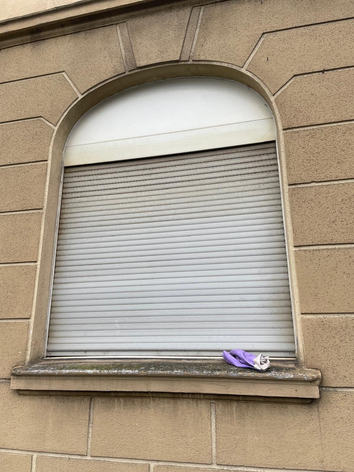 Ein Fenster mit Rollläden und einem lila Tuch auf der Fensterbank.