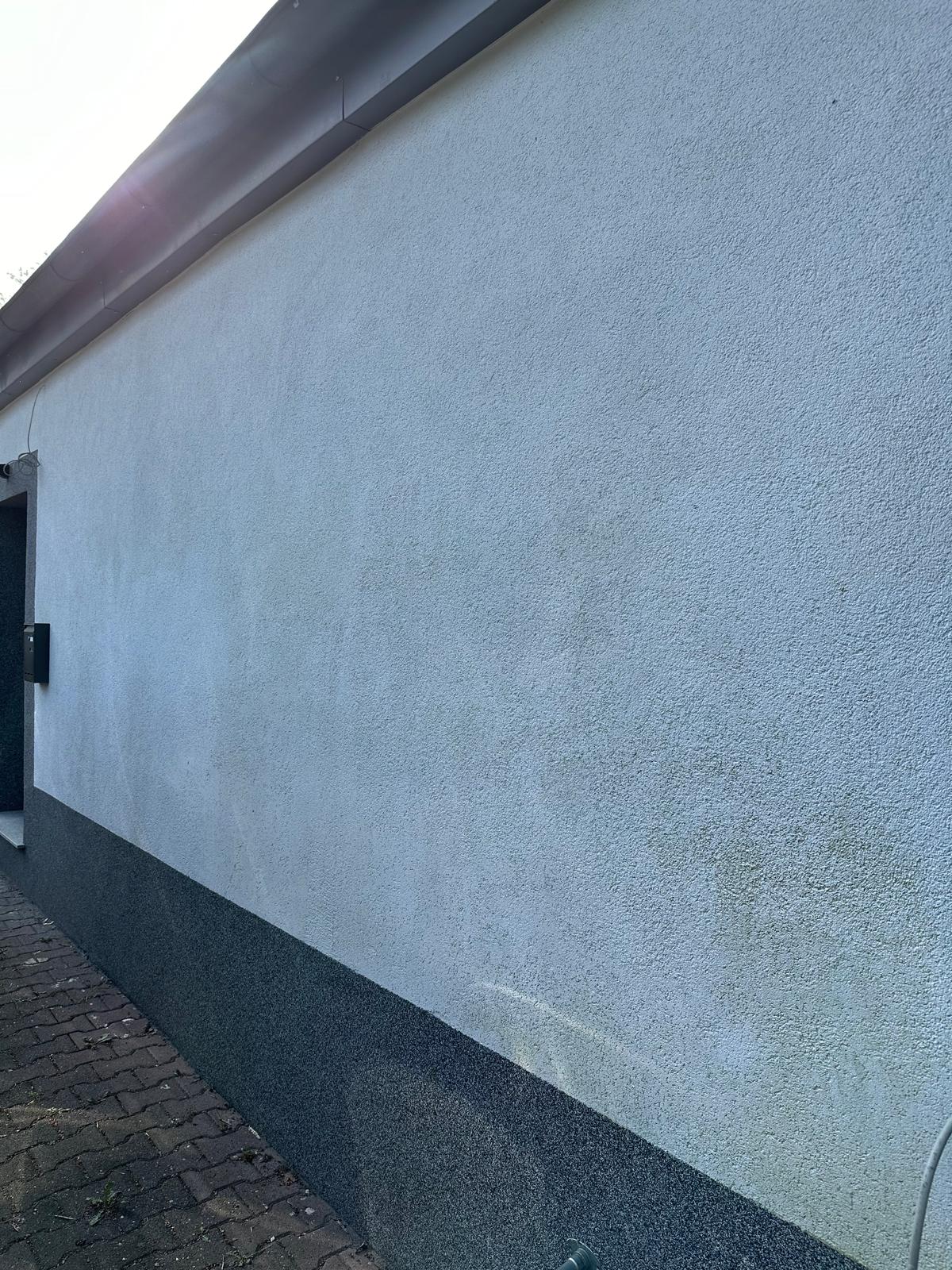 Helle Wand mit grauem Sockel und Pflastersteinen im Vordergrund.