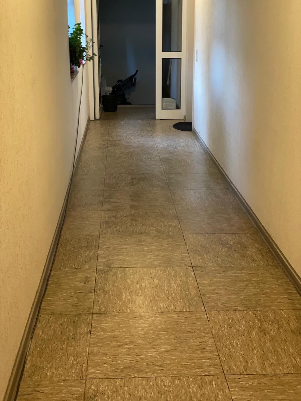 Langer Flur mit grauen Fliesen und einer Tür am Ende.