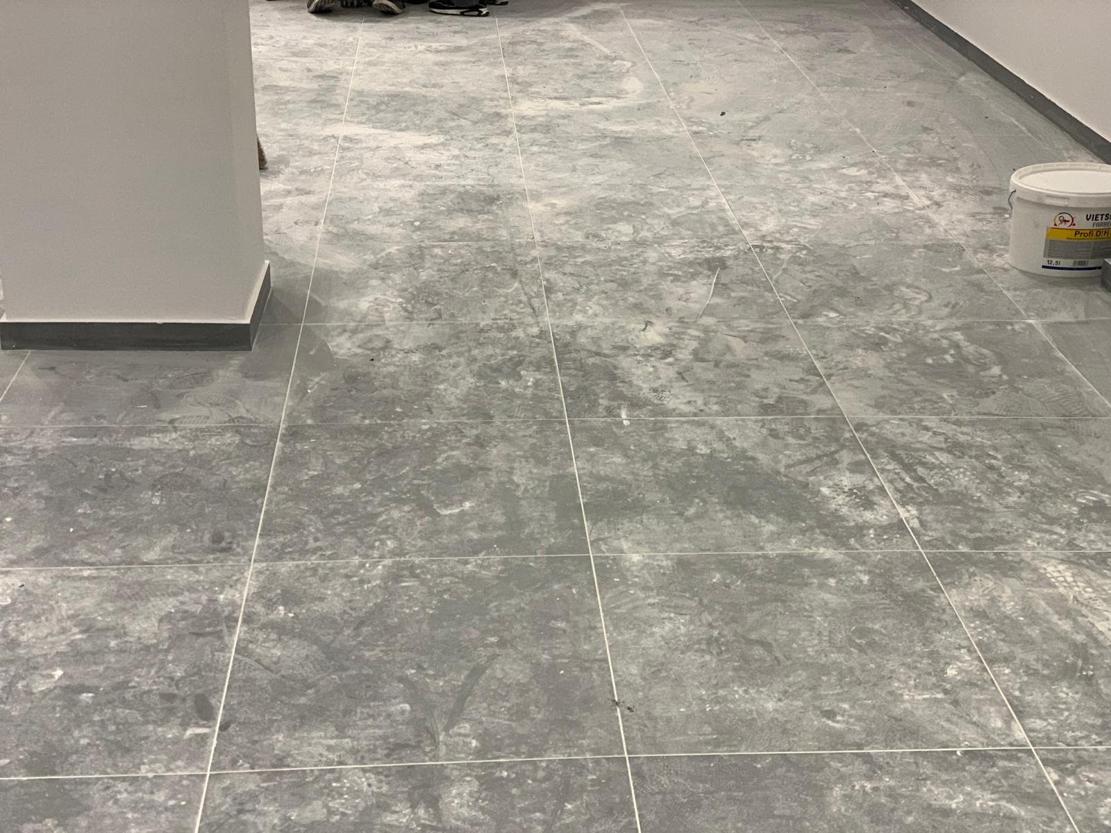 Grau gefliester Boden mit Bauabfällen und Eimer.